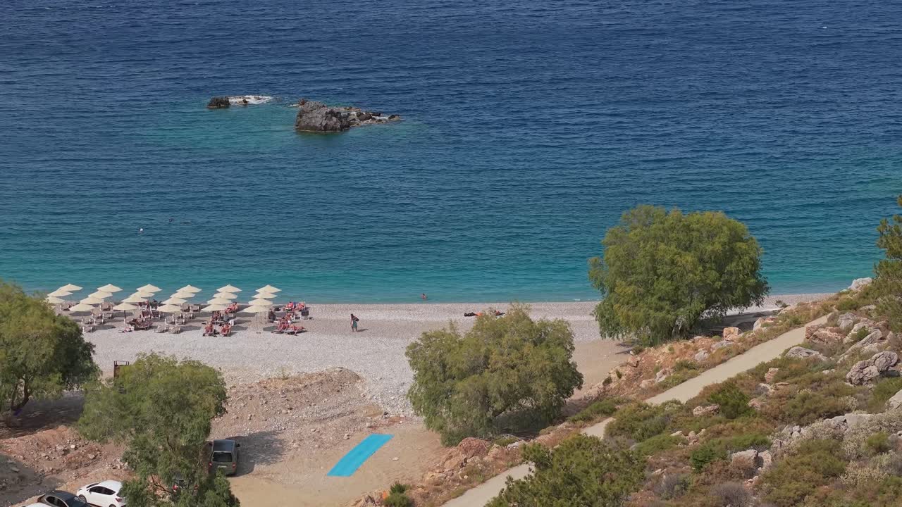 Aerial drone shot revealing Achata Beach in Karpathos, Greece, with pine trees framing the coastline