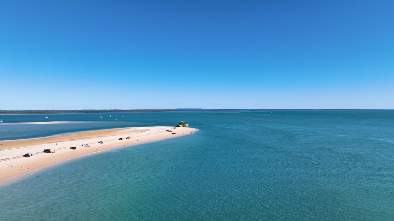 Flight over aqua blue seas to the sandy bar of Queensland's Inskip peninsula, as the K'gari Fraser Island ferry waits at waters' edge with a queue of waiting vehicles. Rainbow Beach Australia