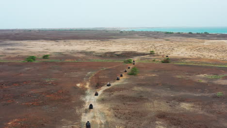 Aerial-shot-of-quad-bikes-driving-through-the-rough-terrain,-during-an-off-road-adventure,close-to-the-coastline