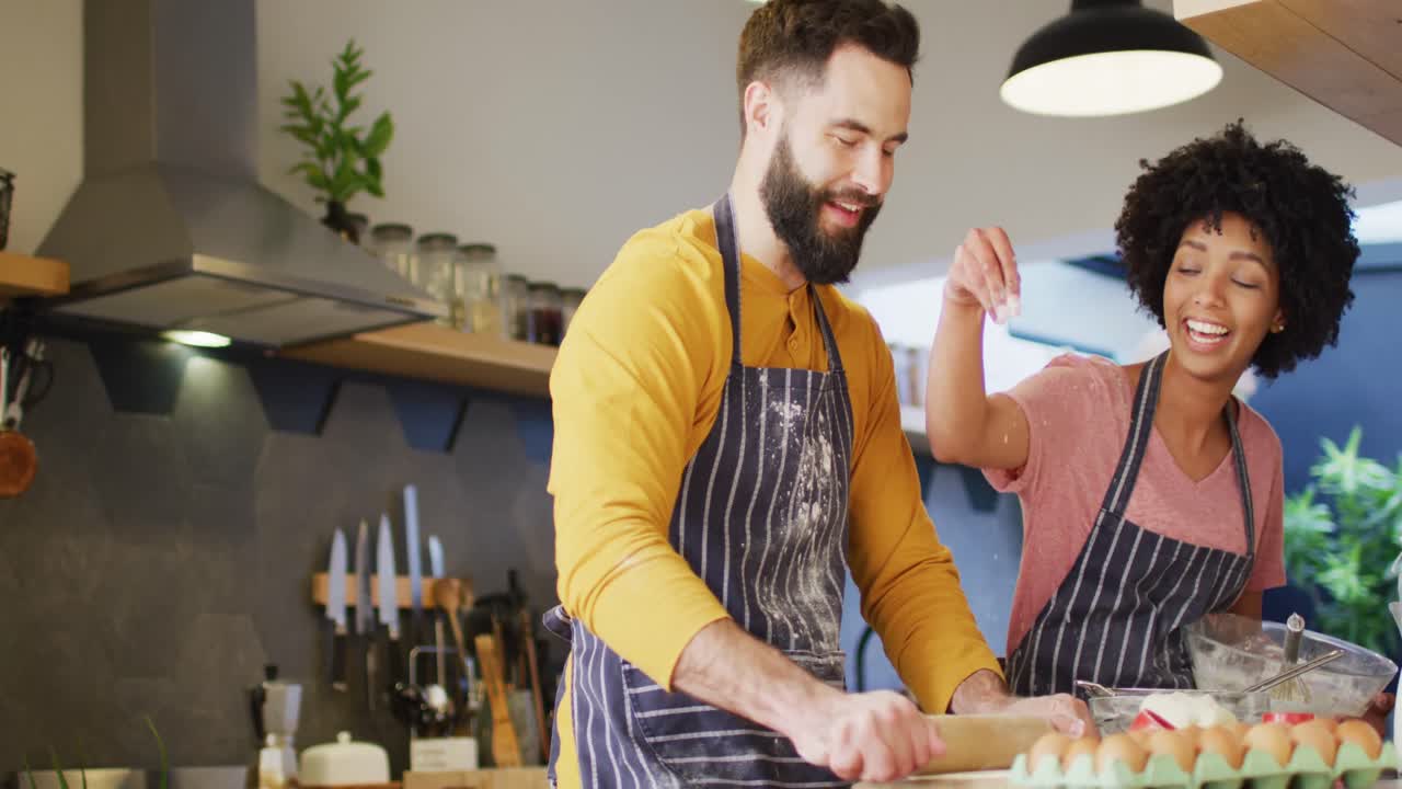 video de una feliz pareja diversa en delantales hablando y horneando juntos en la cocina, con espacio para copiar