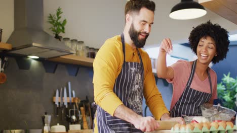 Video-of-happy-diverse-couple-in-aprons-talking-and-baking-together-in-kitchen,-with-copy-space