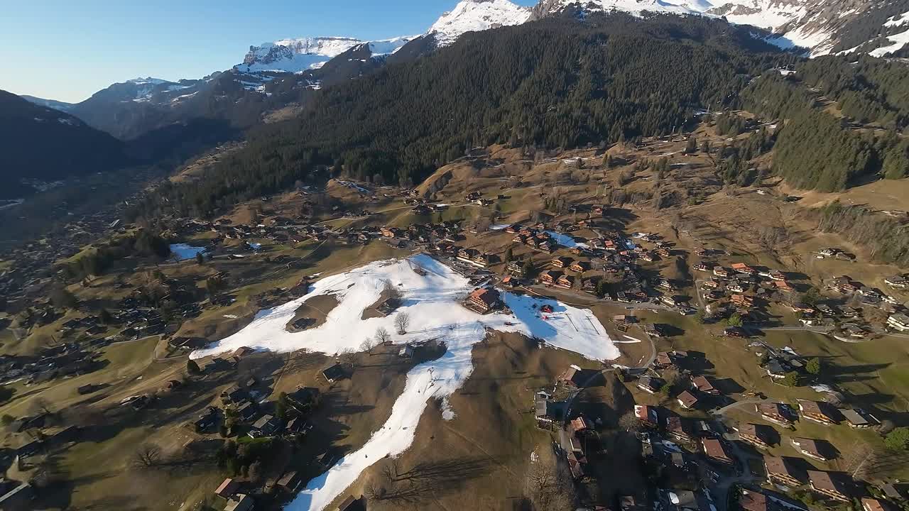 amplia vista aérea de la aldea en los alpes con pistas de esquí cubiertas de nieve en el centro del valle verde