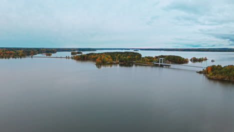 a long suspension bridge crossing a lake along islands surrounded by an autumn forest with green, red yellow and brown trees in valkeakoski, finland