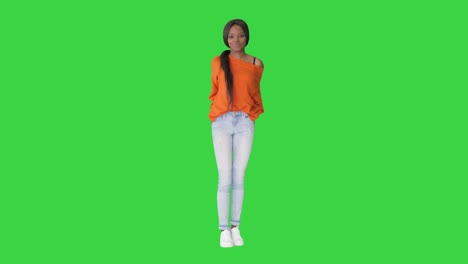 smiling african american woman dressed in bright sweater and jeans posing with her hands in pockets on a green screen, chroma key