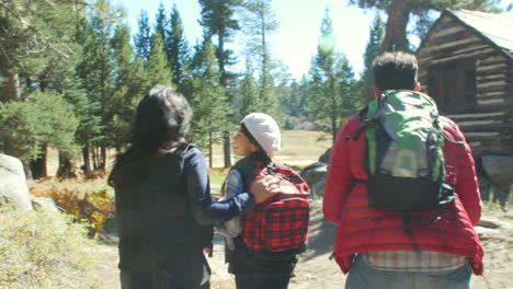 Family-walk-past-cabin-in-a-forest,-dad-puts-son-on-shoulder,-shot-on-R3D