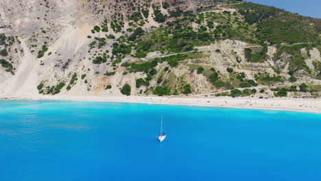 a yacht sailing on myrtos beach turquoise blue waters with limestone cliffs, hairpin roads in background, kefalonia island, ionian sea, panoramic view, drone shot