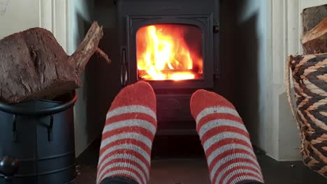 warming up cold feet wearing striped wool hiking socks in front of log burner fire during chilly winters day in cosy, warm house