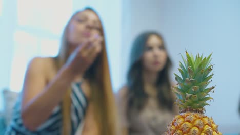 fresh-pineapple-against-blurred-relaxed-women-eating-grapes