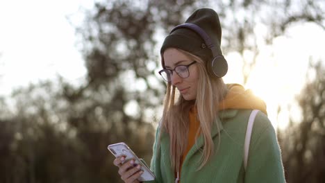 Stilvolles-Mädchen-Geht-Im-Winterpark-Spazieren-Und-Hört-Musik-Am-Telefon-über-Kopfhörer