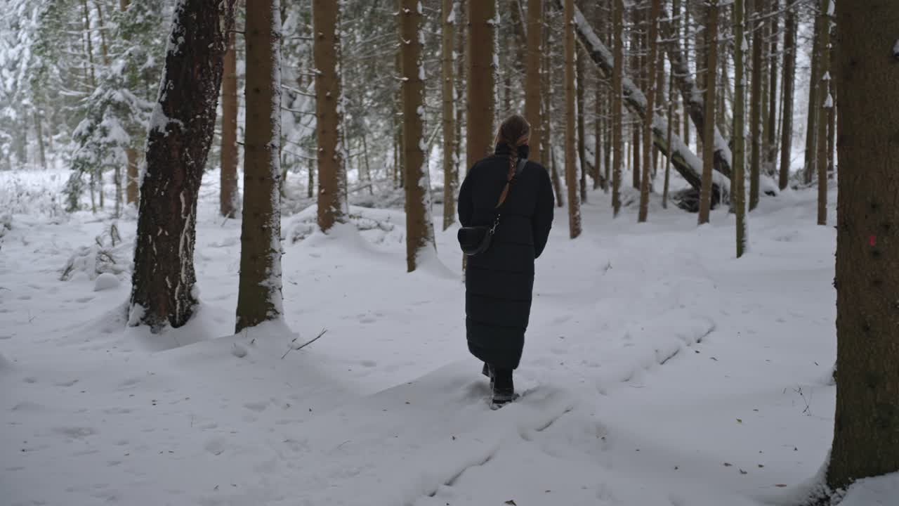 chica con una trenza y en un largo abrigo negro camina a través de la nieve en la naturaleza