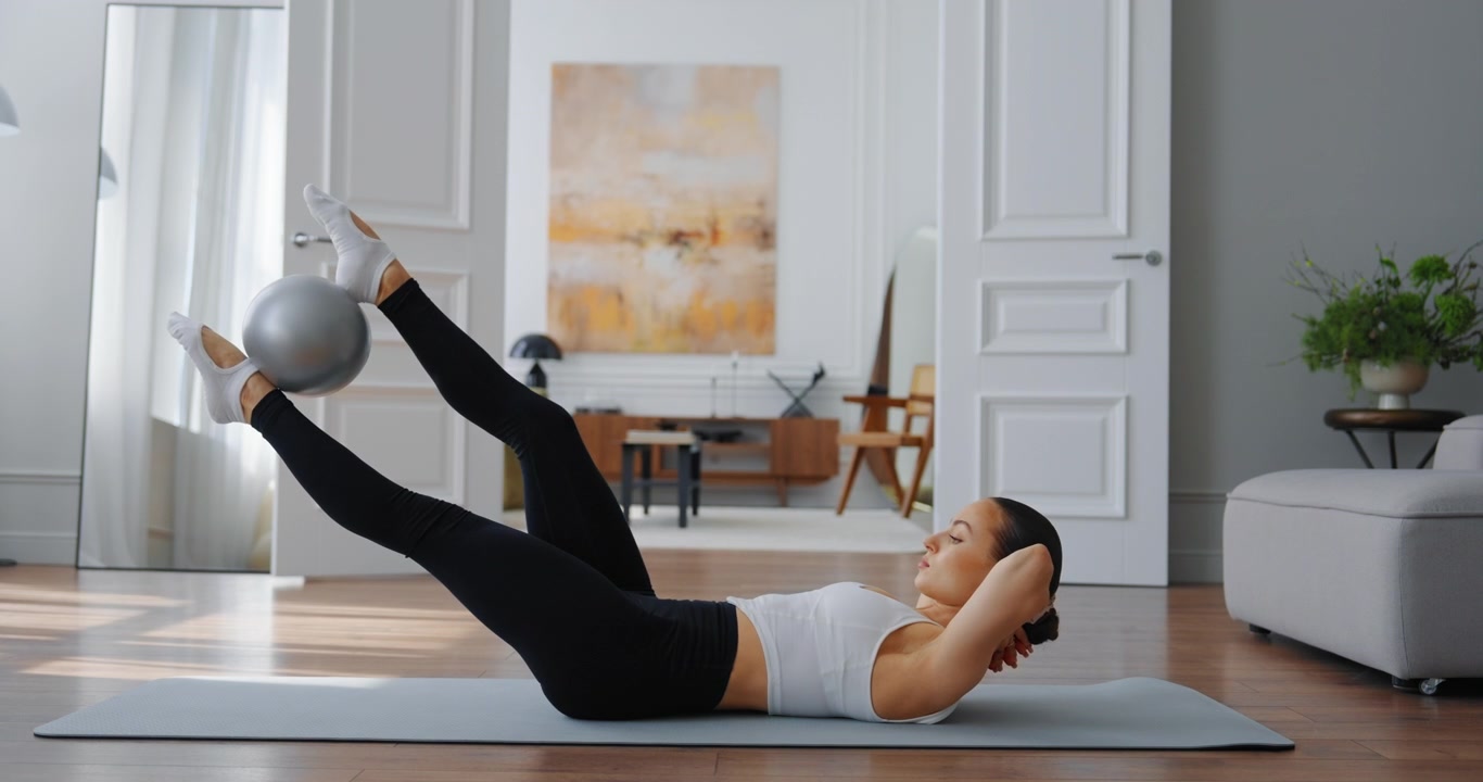 Giovane donna che fa esercizi di Pilates per il core con una piccola palla a casa.