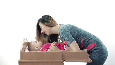 la madre se inclina por encima del bebé en vestido rosa