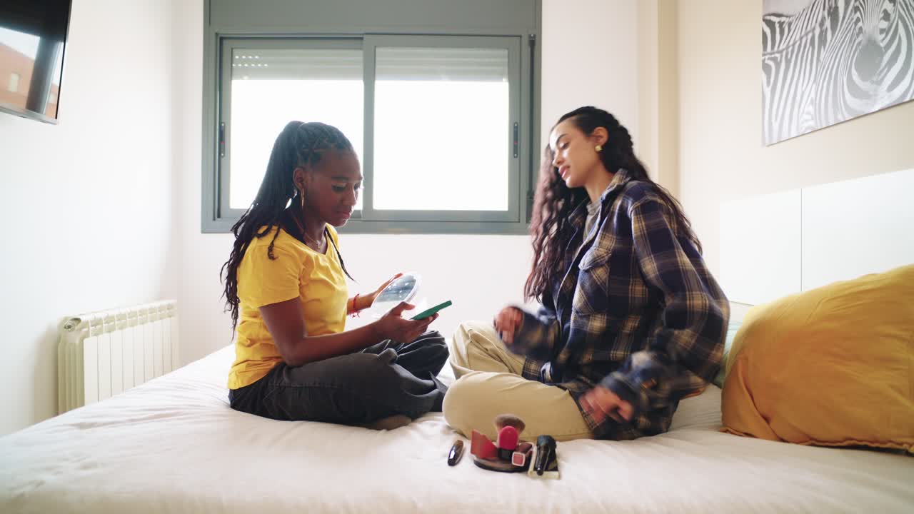 Two women looking at a cellphone on a bed
