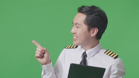 close up of asian man pilot using a tablet and pointing to side while standing in the green screen background studio