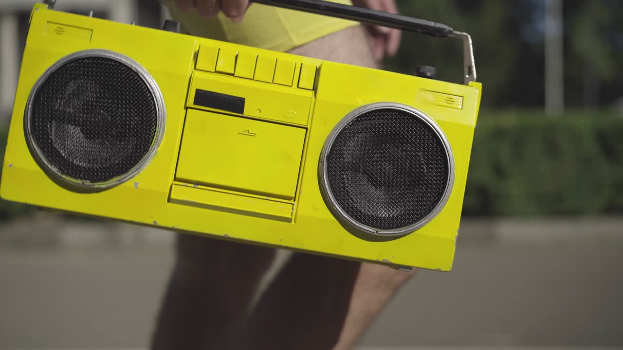 노란색 빈티지 테이프 레코더의 클로즈업, 남성 백인 손으로, 1980 년대 라이프 스타일 콘셉트, 레트로 음악 장치와 함께 은 도시 거리를 따라 걸어가는 인식 할 수없는 남자.