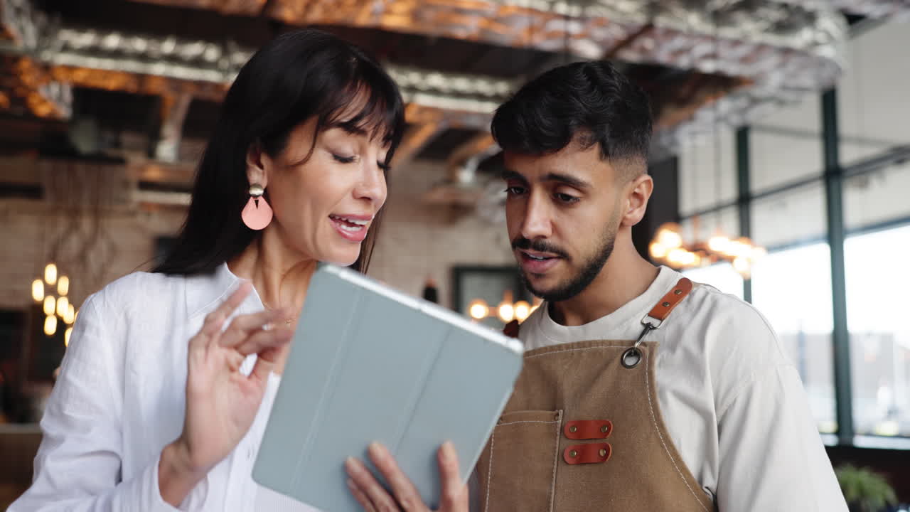 Kvinde og mand diskuterer forretninger på tablet på en café.