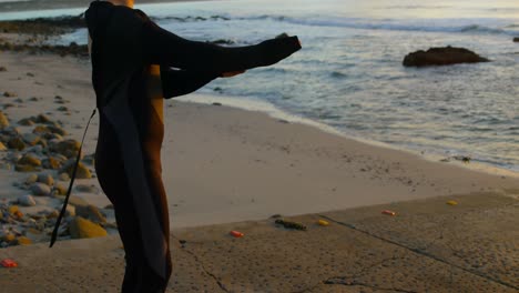 Vista-Lateral-De-Un-Hombre-Caucásico-De-Mediana-Edad-Vestido-Con-Traje-De-Surf-En-La-Playa-Durante-La-Puesta-De-Sol-4k