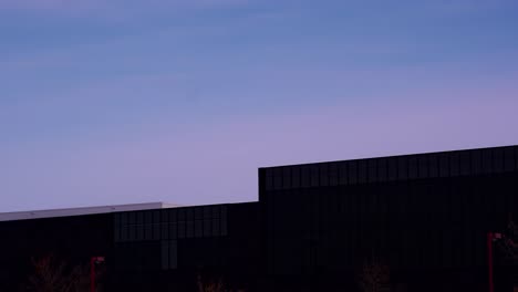 hiperlapso crepuscular de la puesta del sol de un moderno edificio futurista oscuro mientras las nubes ruedan y cambian mientras el clima cambia a una tarde cálida y cálida de nubes blancas a rosas durante este soltice de invierno