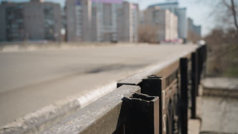 close view of a weathered metal fence along an urban road with a car passing on the bridge and under the bridge in the background