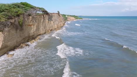 Waves-splash-onto-steep-brown-stone-cliff-in-the-Dominican-Republic,-aerial