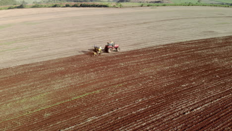 Aerial-view-shot-of-a-farmer-in-tractor-seeding,-sowing-agricultural-crops-at-field