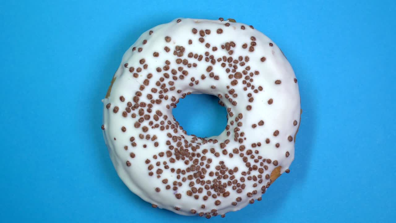 вкусный и свежий посыпанный пончиком крупный кадр макро, вращающийся на синем фоне.