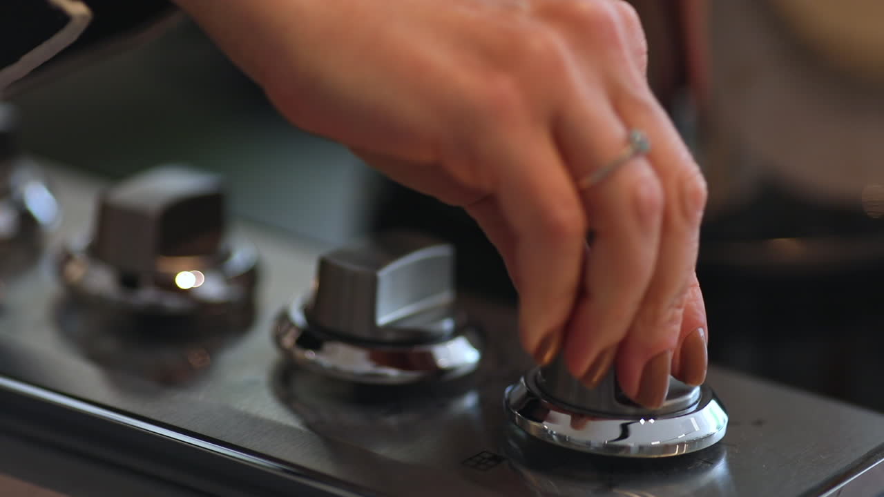 Adult woman sets a pot on the stove and turns the stove on. Close up shot, shallow depth of field.