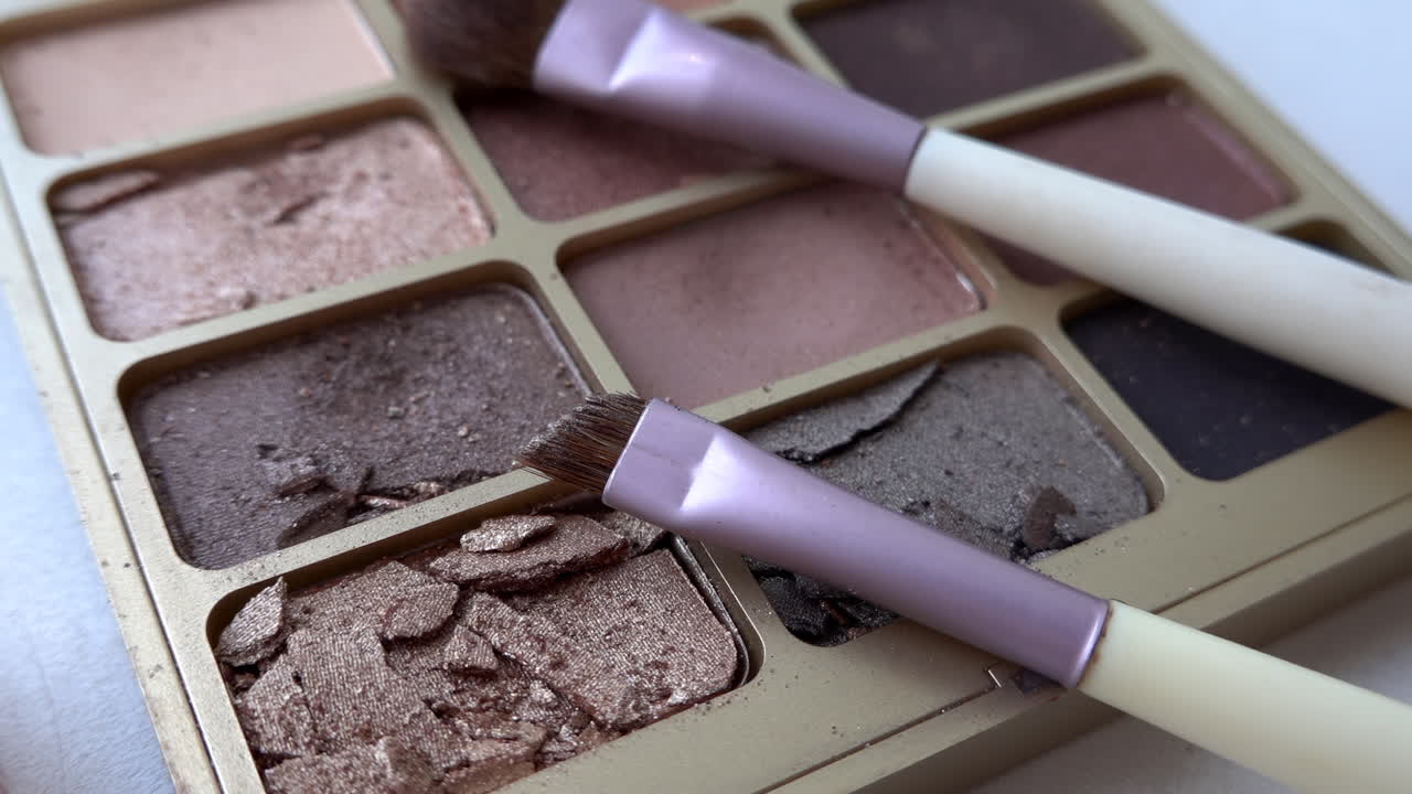 Close up of two purple make-up brushes on an eyeshadow palette