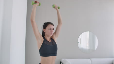 raise the dumbbells over your head performing exercises for the shoulders. training at home in the apartment. a brunette woman with long hair and a beautiful figure