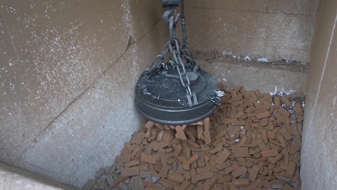 Grúa electromagnética descendiendo en un contenedor de hormigón para recoger palanquillas de acero para la carga del horno