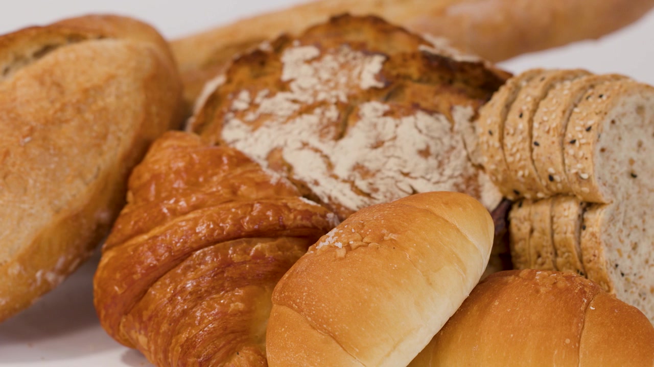 Close-up shot of hands arranging various crusty loaves, croissants, and sliced bread on white.
