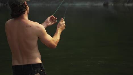 Hombre-Sin-Camisa-Pescando-Con-Mosca-En-Un-Viaje-De-Campamento-Al-Parque-Nacional-De-Los-Glaciares-En-Montana,-Tiro-Bloqueado-Mirando-Al-Hombre-Desde-Atrás-Mientras-Está-Lanzando-Moscas