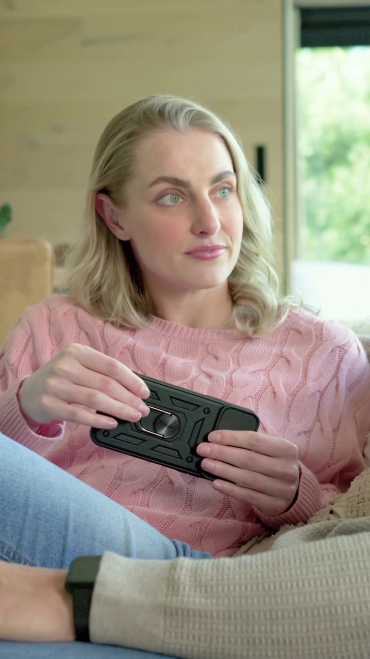Video verticale: Sentendo parlare il partner, una donna con un maglione rosa risponde, toccando l'anello del telefono sul divano.
