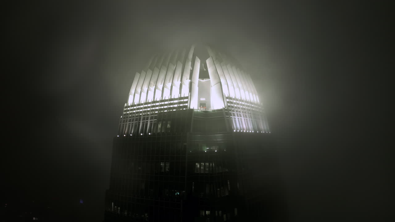 IFC skyscraper in clouds at night illuminated by lights on the top