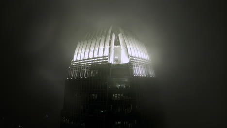 ifc skyscraper in clouds at night illuminated by lights on the top