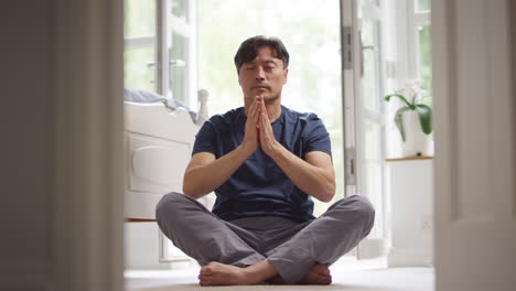 mature asian man in pyjamas sitting on bedroom floor stretching and meditating in yoga pose - shot in slow motion