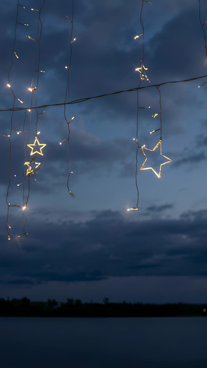 Vertical video: Swaying star LED lights drifting over calm water at dusk, breeze causing twinkling