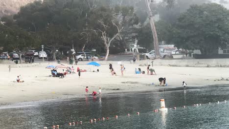 people enjoying dana point beach on a foggy day children playing in the water's white sand with surfers and cabanas in the background hazy surroundings static
