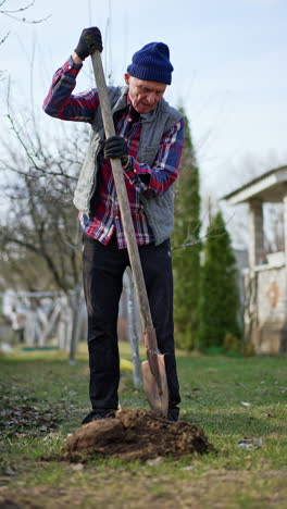 male farmer in checkered shirt and vest uses a shovel to dig the ground. low angle view at the gardener working in his garden. vertical video.