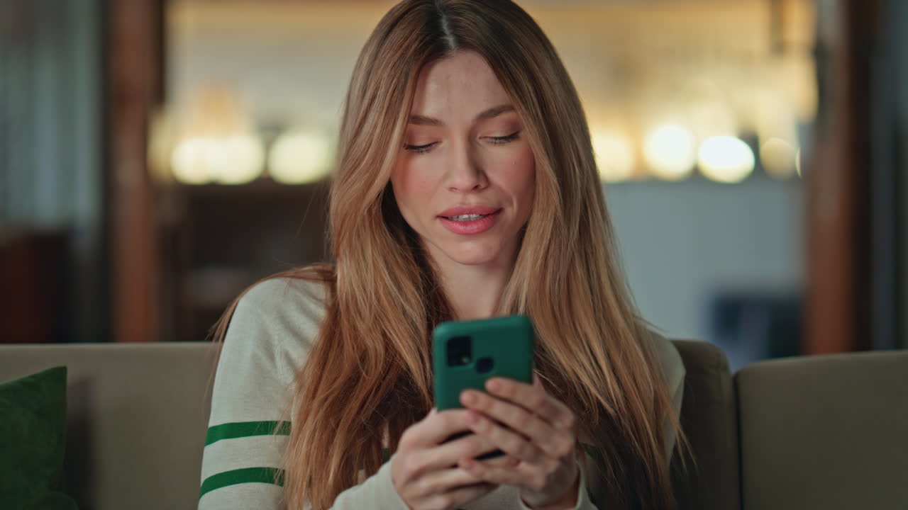 Donna risponde al messaggio dello smartphone rilassandosi nel soggiorno dell'appartamento, primo piano