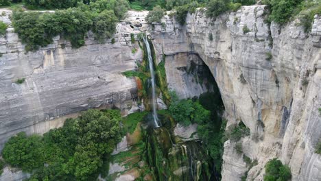 pared de roca empinada, cascada estrecha y alta, subida para revelar la vista aérea del bosque