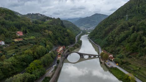 a serpentine river with a bridge in tuscany, lush greenery on both sides, cloudy day, aerial hyperlapse