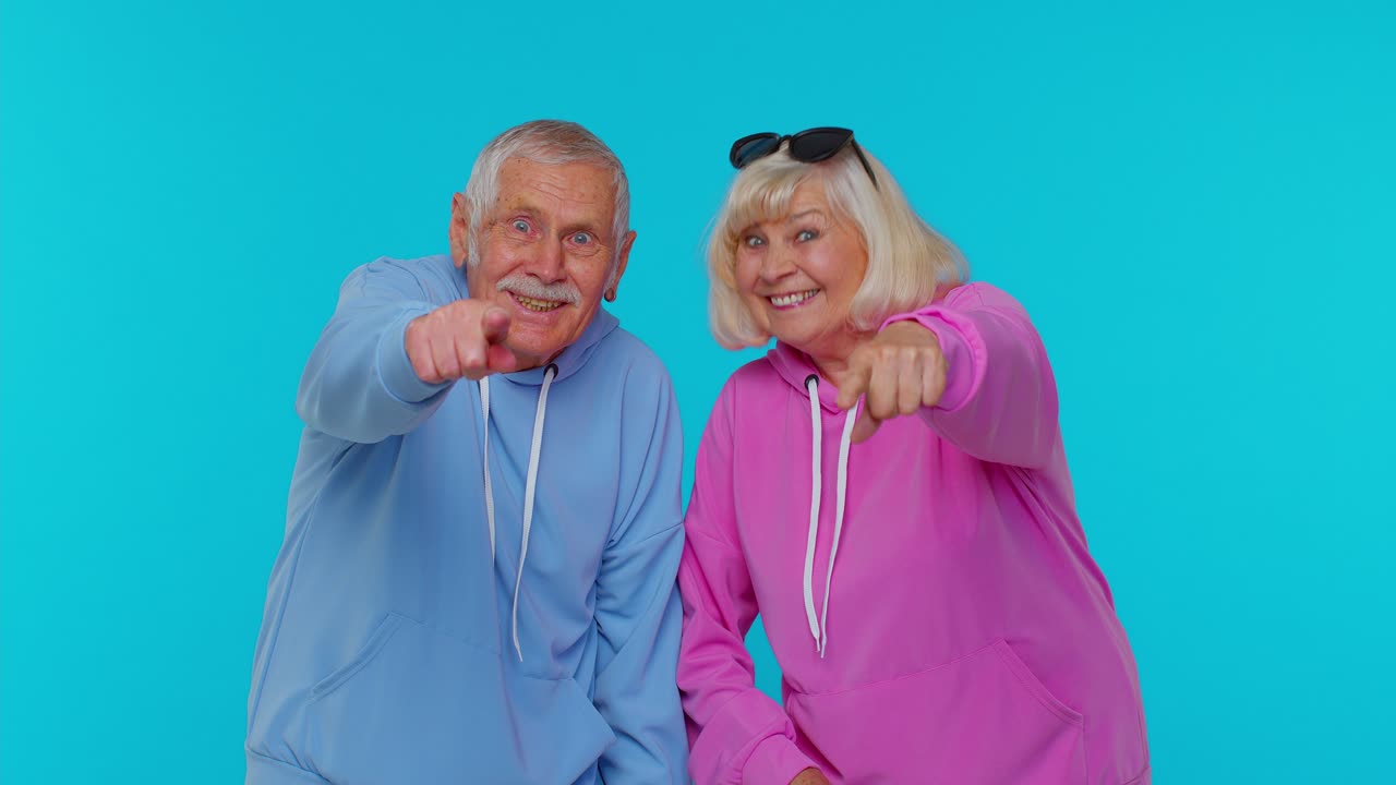 Amused senior couple man woman grandparents pointing finger to camera, laughing out loud, funny joke