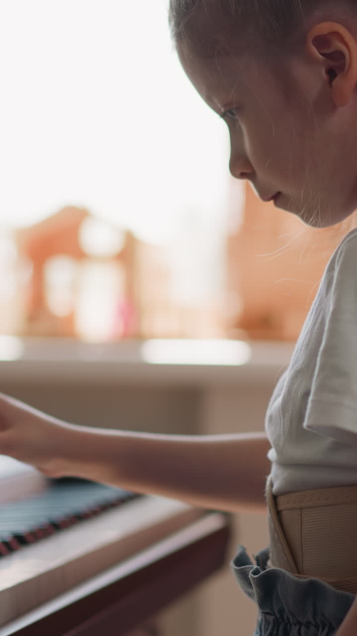 Diligent girl plays electronic piano with right hand. Schoolgirl wearing corset masters technique of playing with long and short notes side view on blurred background
