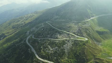 a dramatic serpentine road winds its way through a rugged mountain landscape, dotted with rocks and sparse vegetation. several cars are visible navigating the curves.