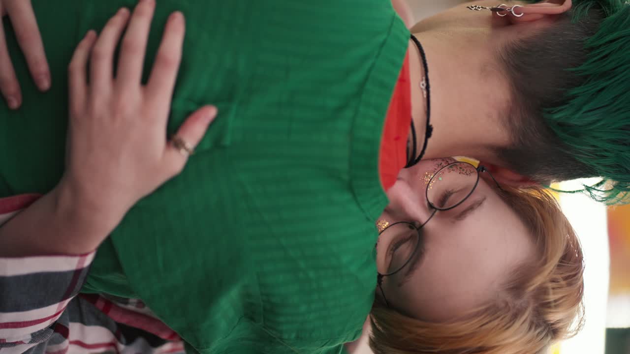 video vertical: una suave chica rubia con un corte de pelo corto abraza a su novia con un corto corte de pelo verde en una camisa verde durante su cita en el parque de atracciones