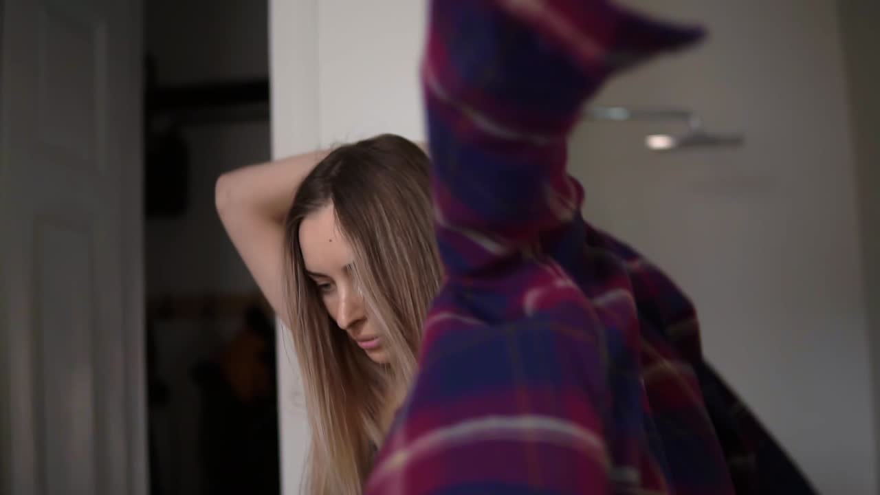 금발 여자 가 옷장 에서 옷 을 선택 하고, 체크 된 셔츠 를 입고 있다