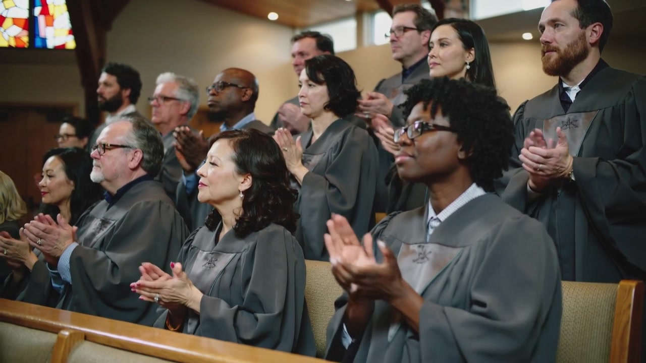 Membri del coro che applaudono in risposta al sermone conclusivo tra i banchi della chiesa, mostrando l'emblema sulle vesti grigie.