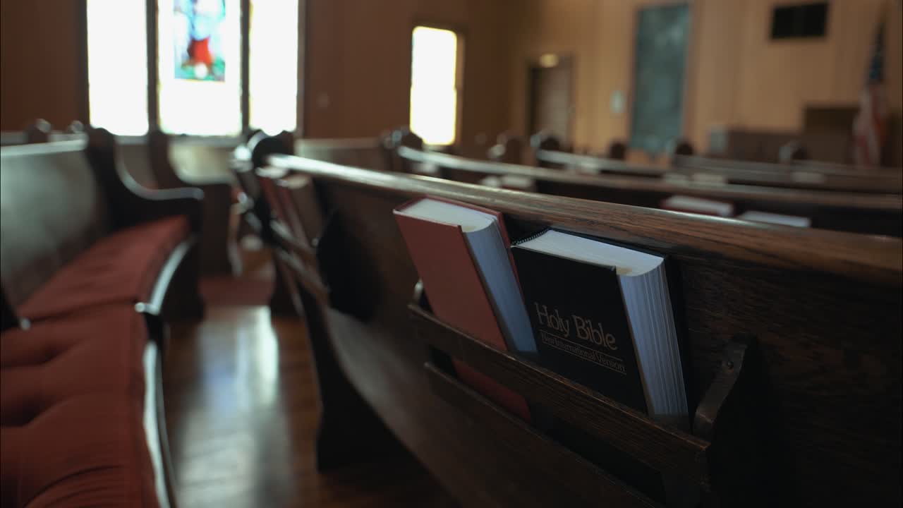 Close-up of wooden church pew with a Holy Bible and hymn book placed in the holder. The scene highlights faith, worship, and the sacred atmosphere of a traditional church interior