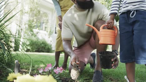 una feliz pareja afroamericana con un hijo plantando flores en un jardín soleado, cámara lenta
